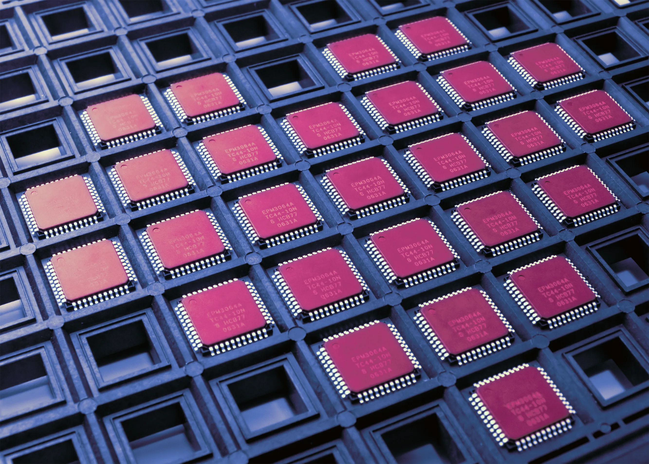 Macro view of dozens of magenta-pink integrated-circuit chips arranged in a black anti-static tray. The high-value, security-sensitive electronics cargo class flowing through Port Newark Container Terminal — semiconductors, circuit boards, electric motors, optical and medical instruments — with chain-of-custody and BIS Entity List compliance handling.