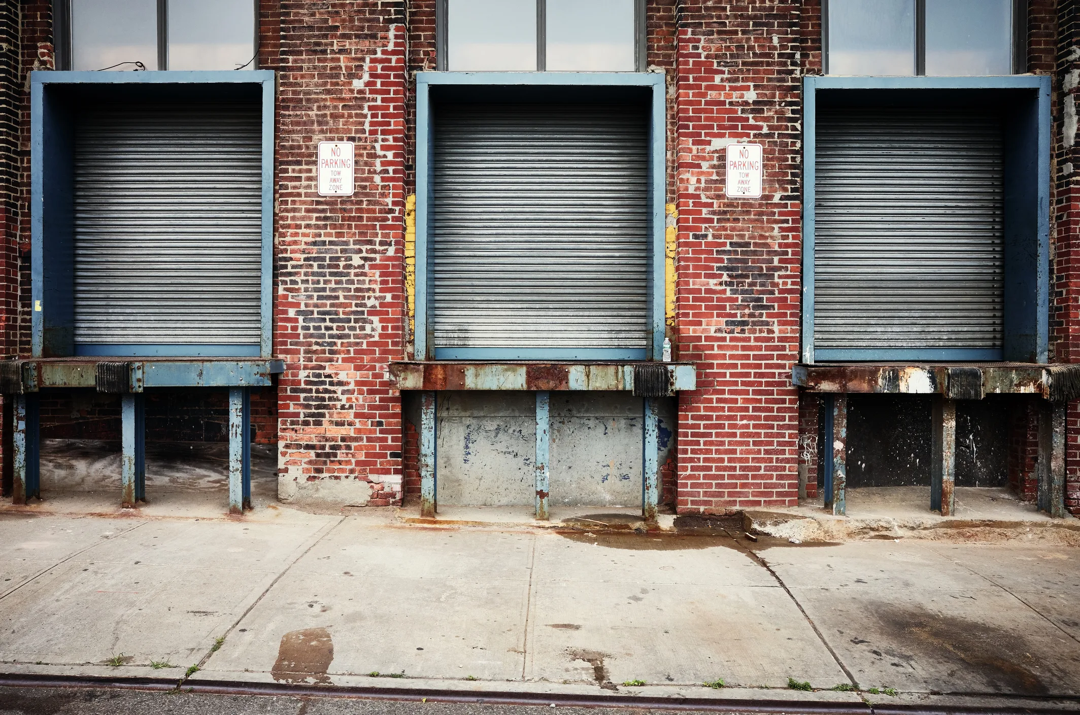 Three loading dock bays in a classic NYC industrial building — blue-painted dock frames against aged red brick, concrete platforms, the working infrastructure where freight actually moves